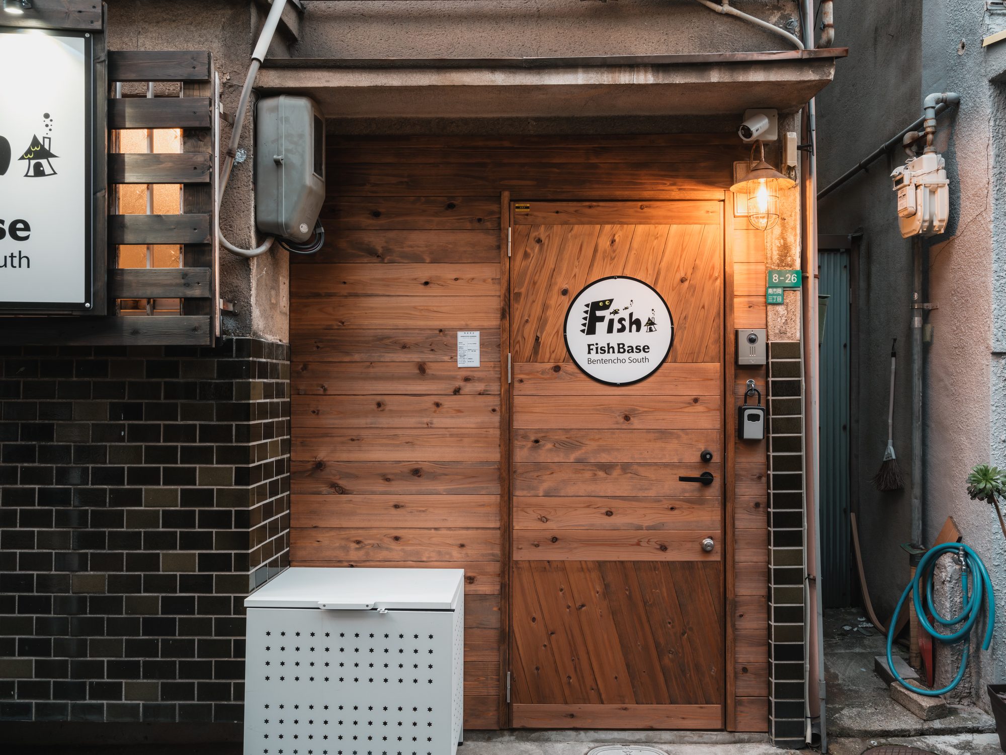 Fish Base 弁天町南の外観。細い路地の奥にある木製の玄関ドアと看板
